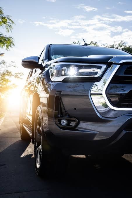 Black SUV parked outdoors with sunlight glowing from behind, against a blue sky with white clouds