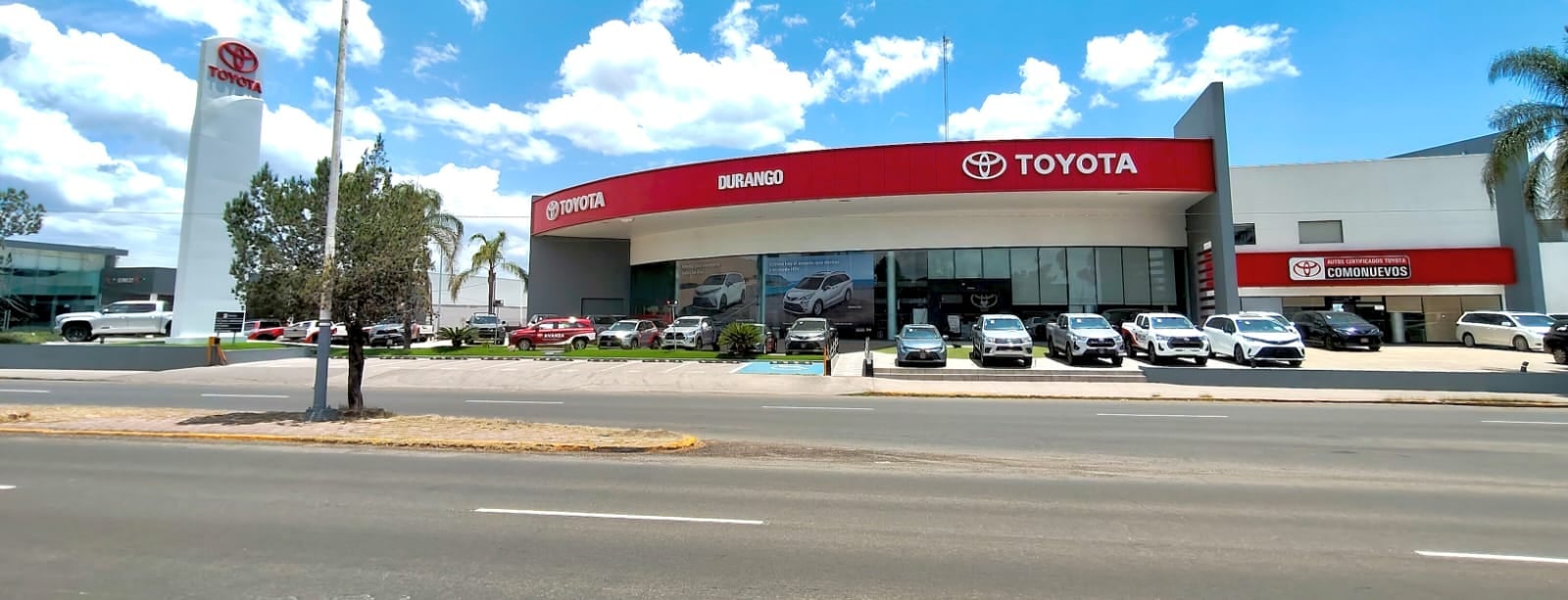 Toyota dealership building with red and white exterior, vehicles parked outside, palm trees, and street view