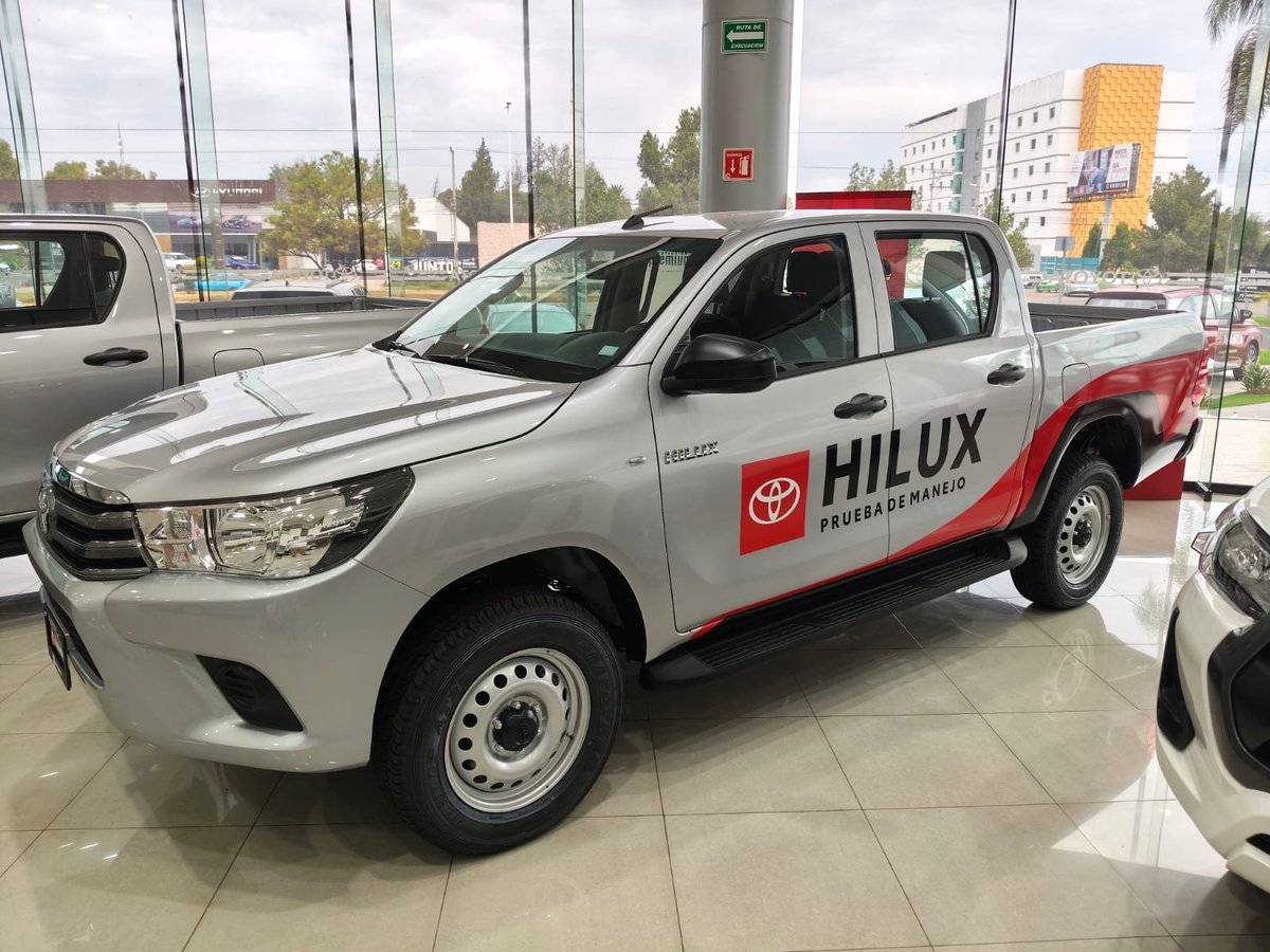 White Toyota Hilux pickup truck on display at a dealership showroom with glass windows visible in background