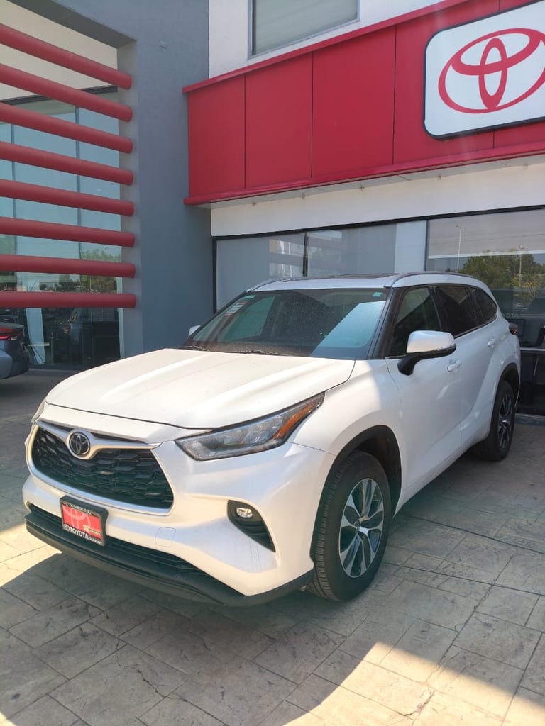 White Toyota Highlander SUV parked in front of a Toyota dealership with red signage and logo