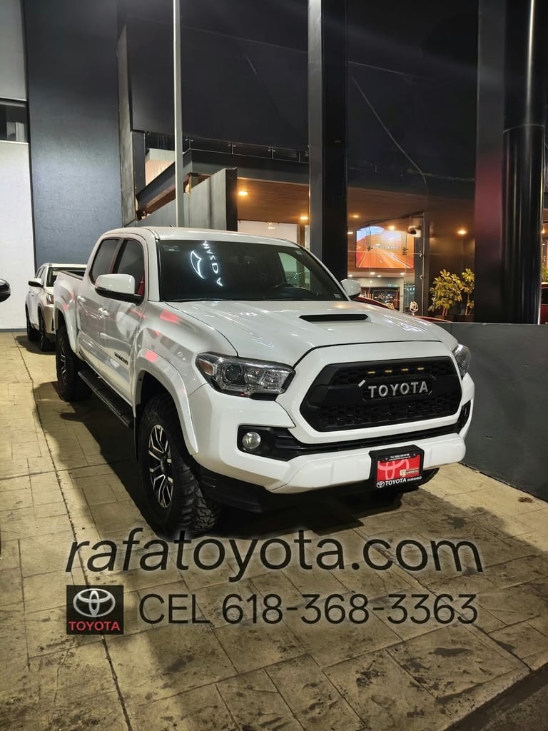 White Toyota pickup truck parked at night outside a dealership with logo and contact information visible