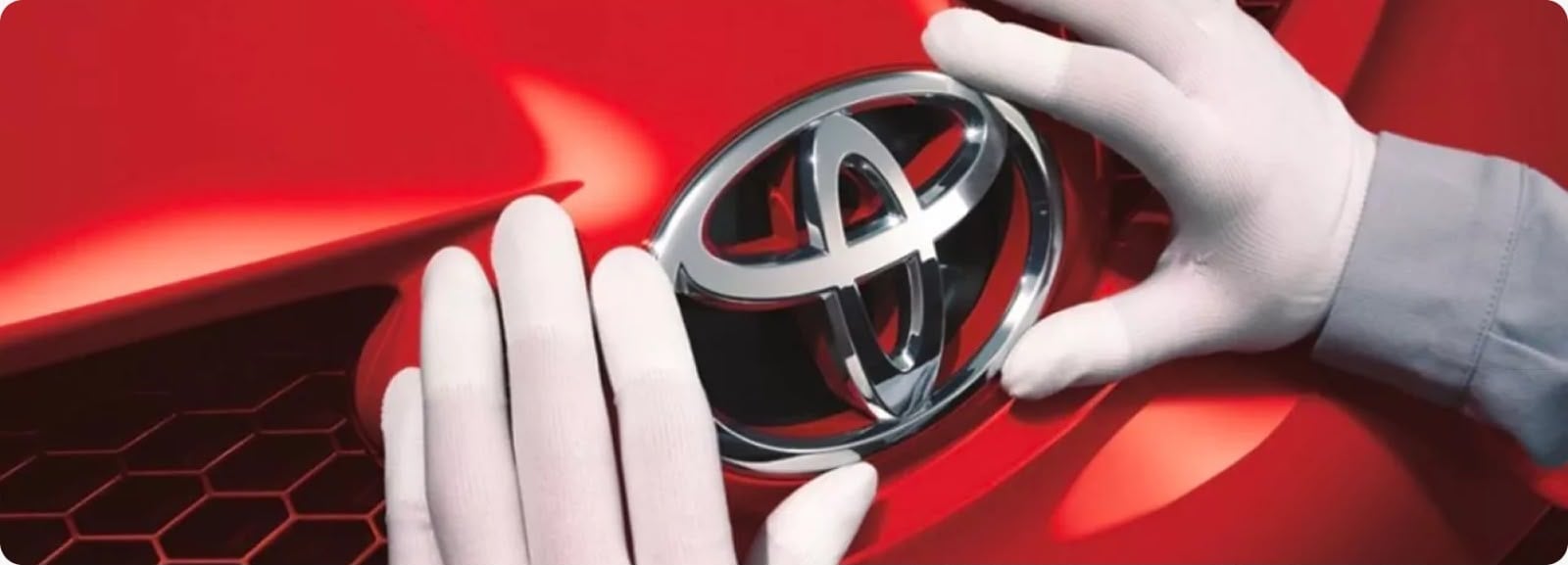 Hands holding a silver Toyota logo against a red car grille background
