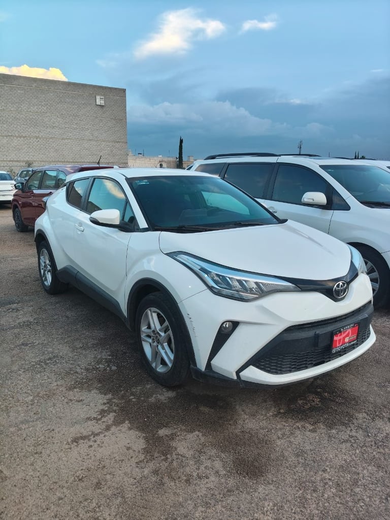 White Toyota C-HR parked in a lot with other vehicles and a brick building in the background