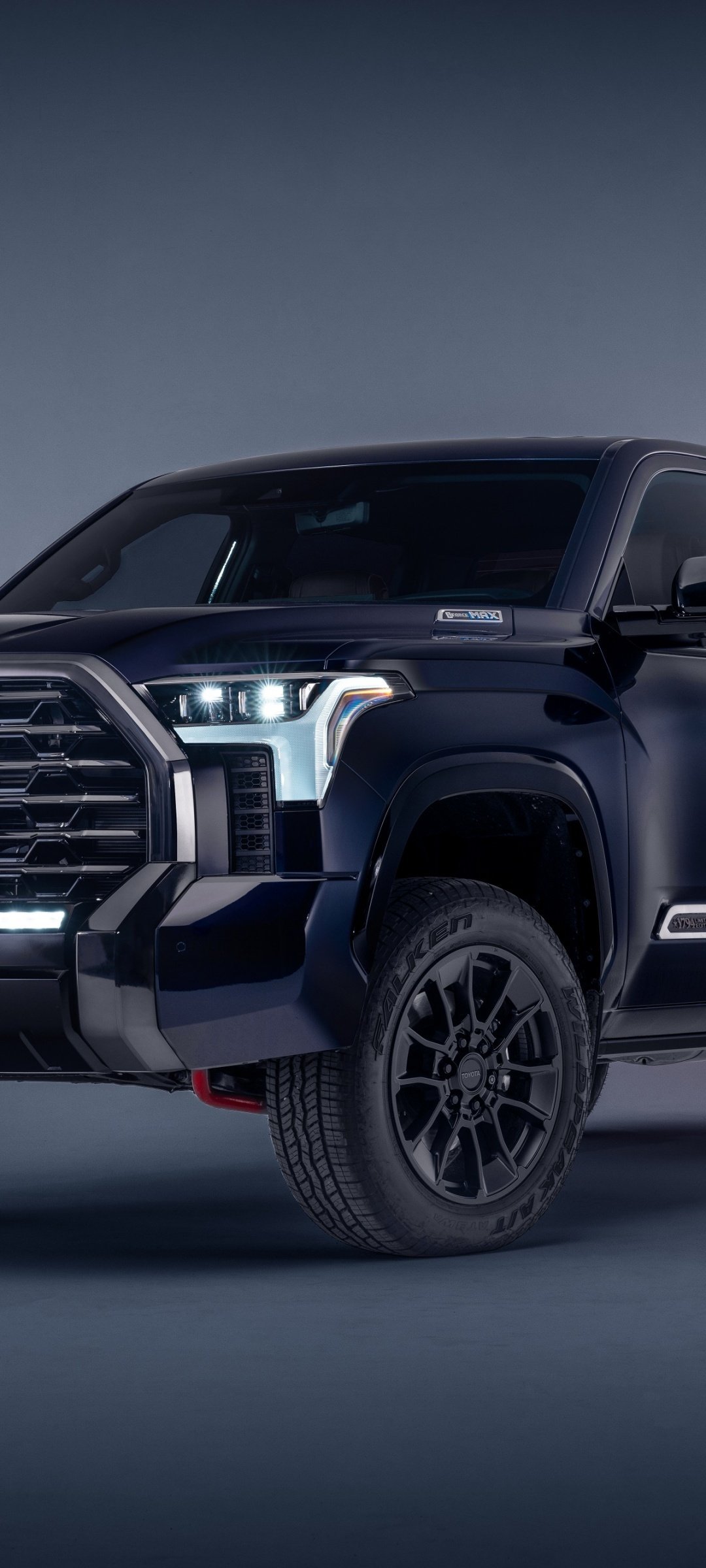 Front-angled view of a black full-size pickup truck with LED headlights and alloy wheels against a blue gradient background