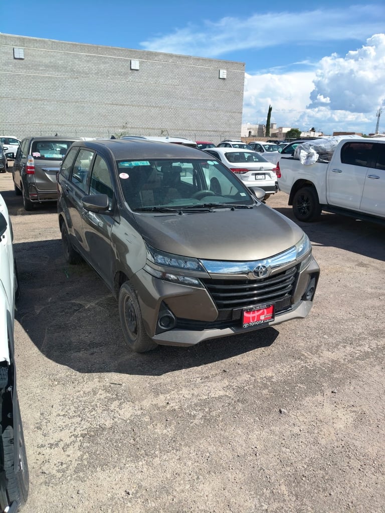 Gold Toyota minivan parked in a car lot with other vehicles and a brick building in the background