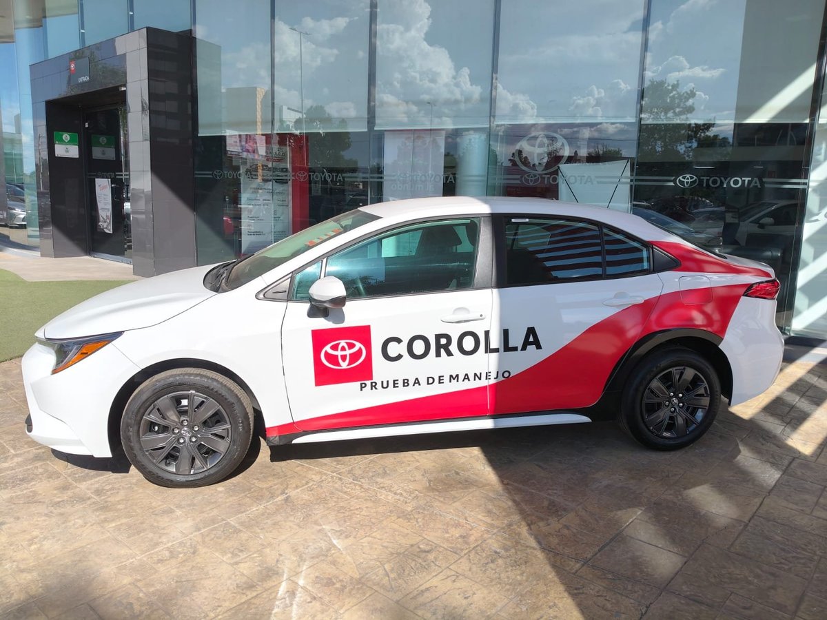 White and red Toyota Corolla with promotional wrap parked outside a dealership showroom