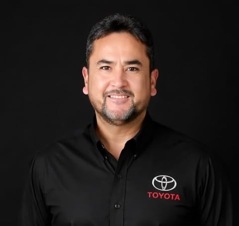 Professional headshot of a man wearing a black Toyota-branded polo shirt against a dark background