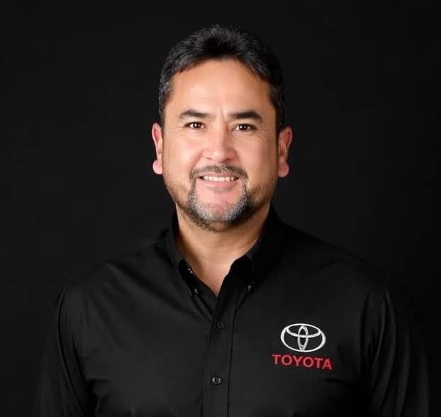 Professional headshot of a man wearing a black Toyota branded polo shirt against a dark background